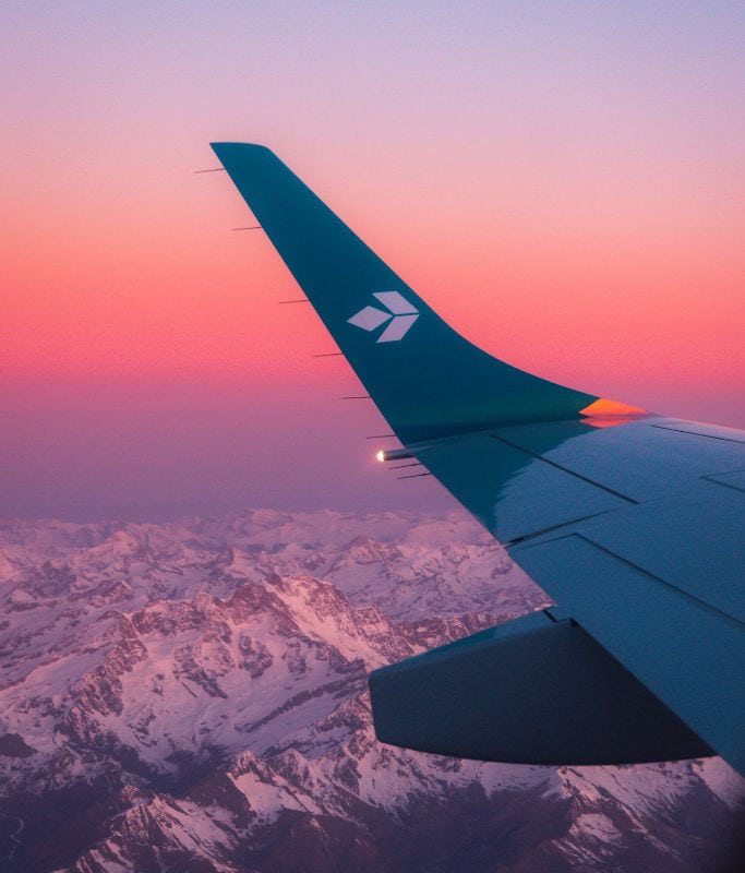 A picture of a plane flying at sunset over the mountains.