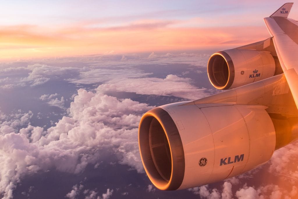 A picture of a KLM plane flying over clouds during sunset.