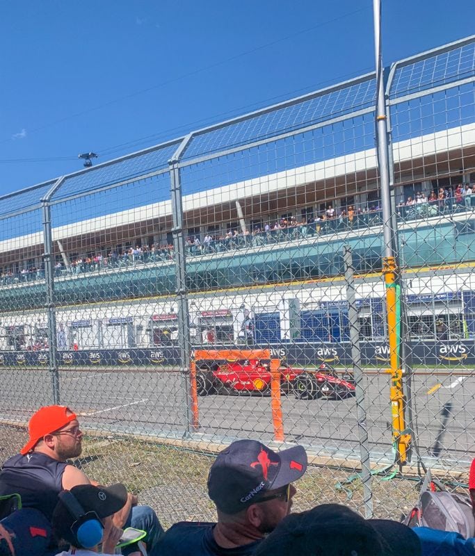 A picture of Charles LeClerc racing by and the view from the general admission area that is to the left of grandstand 1.