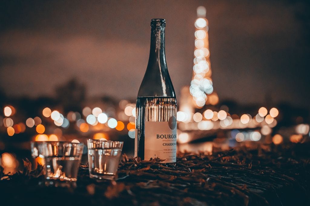 A picture of a bottle of wine and two glasses with the Eiffel Tower shimmering in the background.