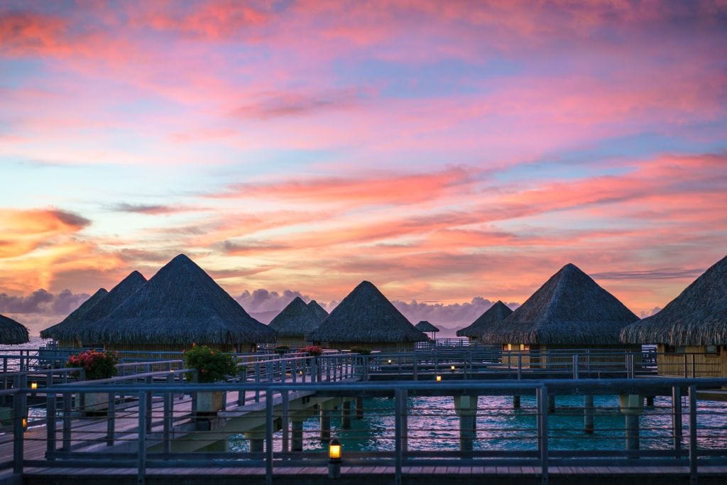 A picture of overwater bungalows in French Polynesia with a beautiful pink and orange sunset.