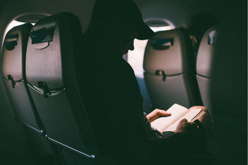A picture of a man reading a book. Everyone, not just first time flyers, should bring their own in-flight entertainment in case the plane doesn't have any.