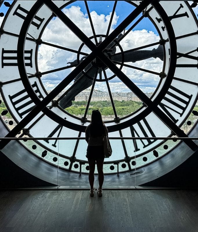 A picture of Kristin standing in front of the iconic clock within  Musee d'Orsay.