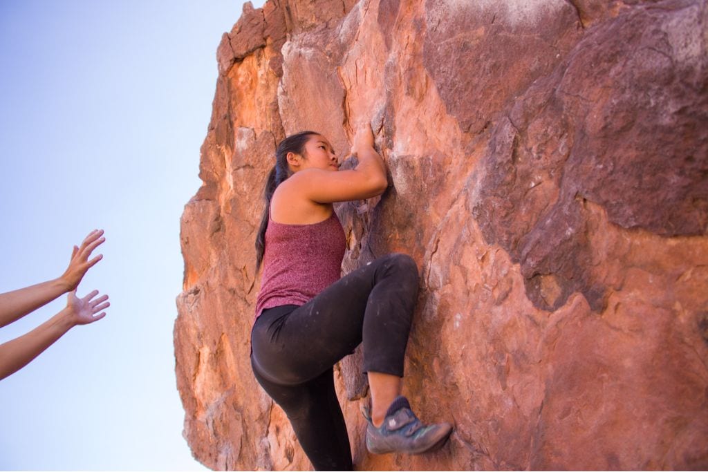A picture of Kristin bouldering and someone spotting her.