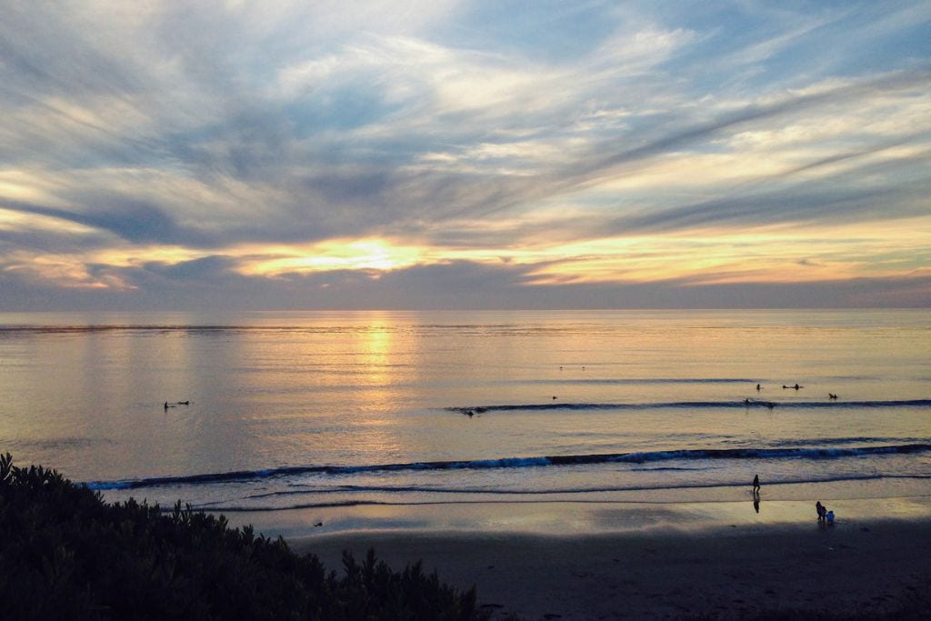 A picture of a light blue-yellow sunset at San Elijo state Beach. You can also see some surfers in the water.