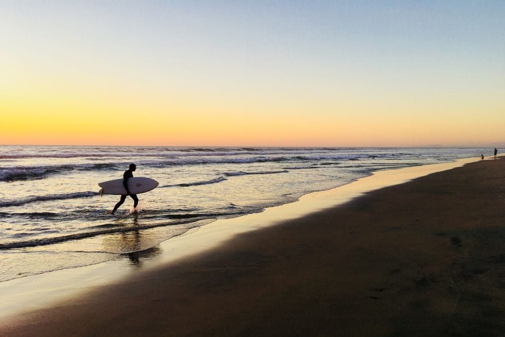 Picture of a surfer exiting the ocean at La Jolla Shores, one of the most popular surfing spots in San Diego for beginners.