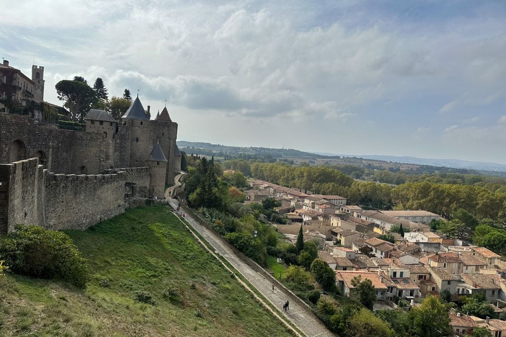A picture of the hill leading up to the Cité de Carcassonne. On the left side you can see the medieval walls and on the right, you can see some of the buildings in Old Town.