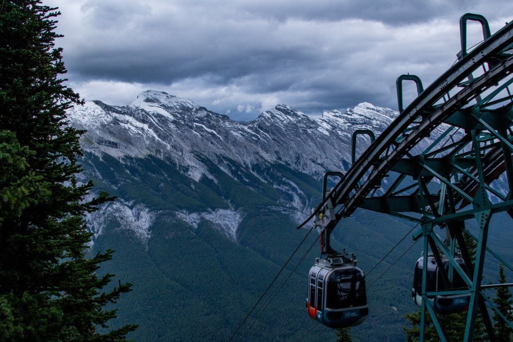 A picture of the Banff Gondola with a dramatic backdrop of the Canadian Rockies in the background. Riding the Gondola is fantastic alternative if you don't want to hike up Sulphur Mountain on the final day of your 4-Day Banff Itinerary.