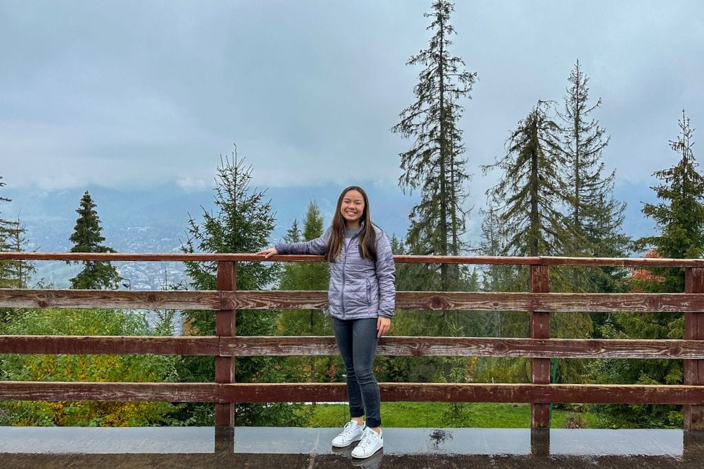 A picture of Kristin smiling with the Tatra mountains and pretty trees in the background.