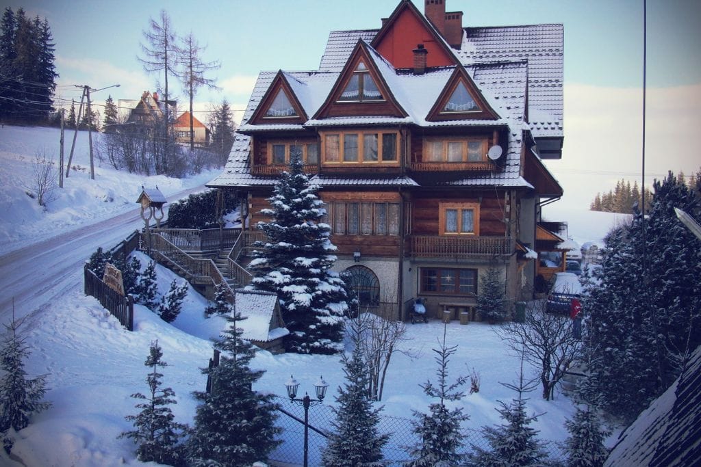 A picture of a wooden chalet that features Zakopane-style and is covered with snow. For those who take a Zakopane Tour from Krakow during the wintertime, you'll see lots of snow in the mountains.