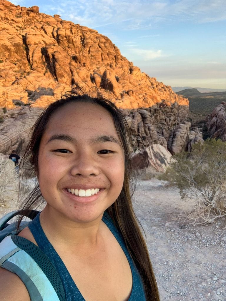 A picture of Kristin smiling with her backpack and the beautiful red rocks in the background. Doing a bike tour through Red Rock Canyon is one of the best ways to intimately see the views!