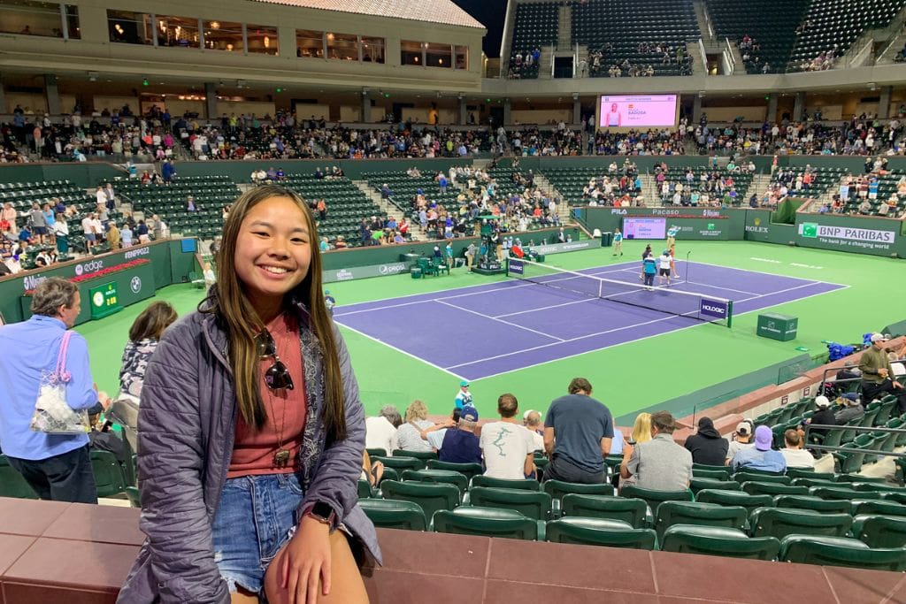 A picture of Kristin smiling while sitting on a ledge in Stadium 2 at the Indian wells tennis tournament