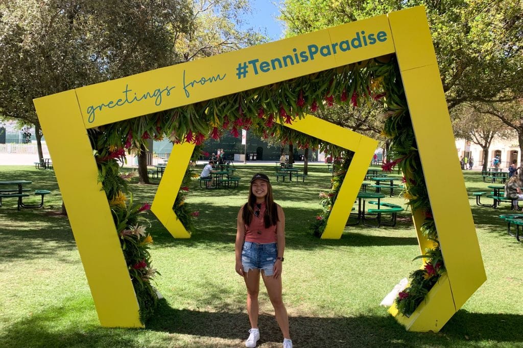 A picture of Kristin standing under a yellow frame that says #tennisparadise at the Indian wells tennis tournament