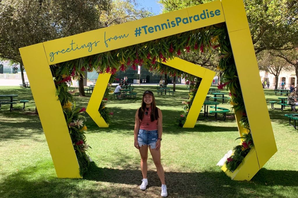 A picture of Kristin standing underneath a yellow arch at the BNP Paribas Open in Palm Springs.