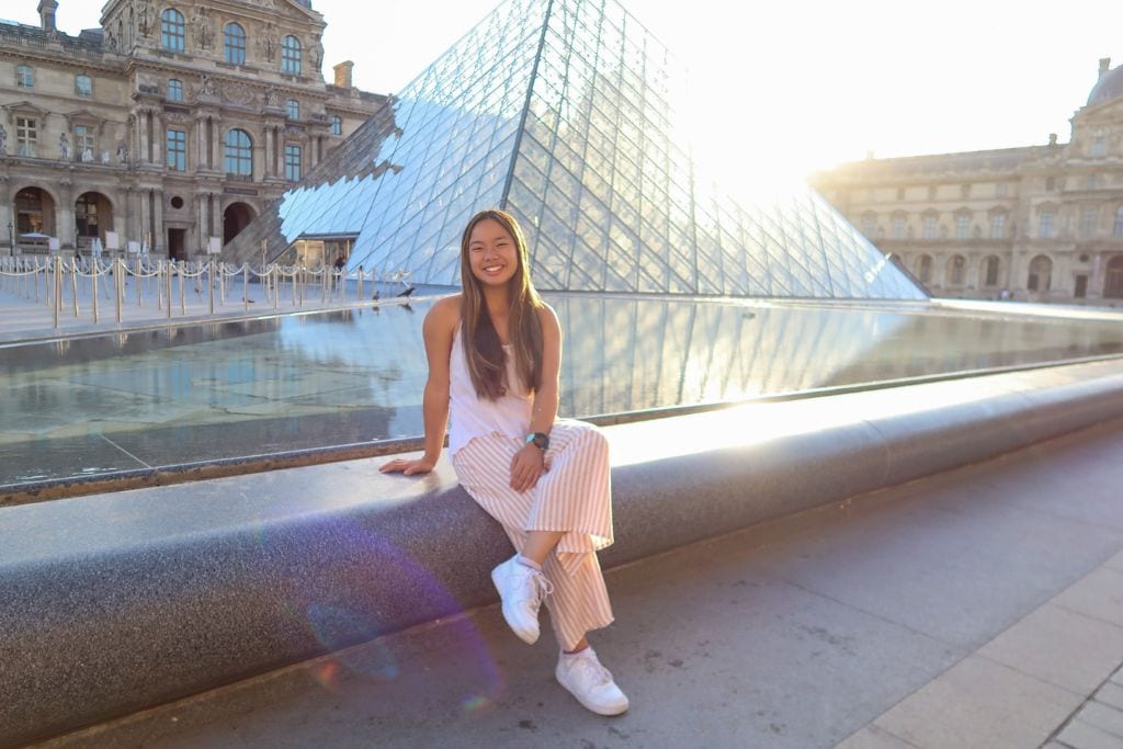A picture of Kristin sitting in front of the Louvre during an early morning photoshoot. When comparing Paris vs Milan, Paris has more architecturally diverse spaces!