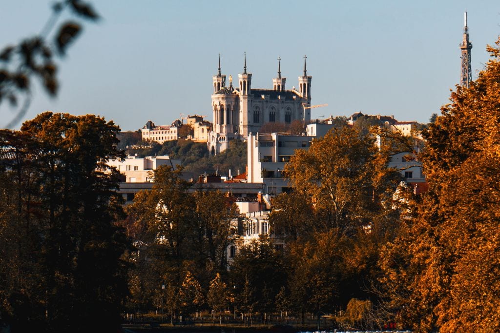 A picture of Lyon's Basilica from a distance. The trees are auburn, which indicates it's fall and not quite the season for seeing any snow in Lyon France.