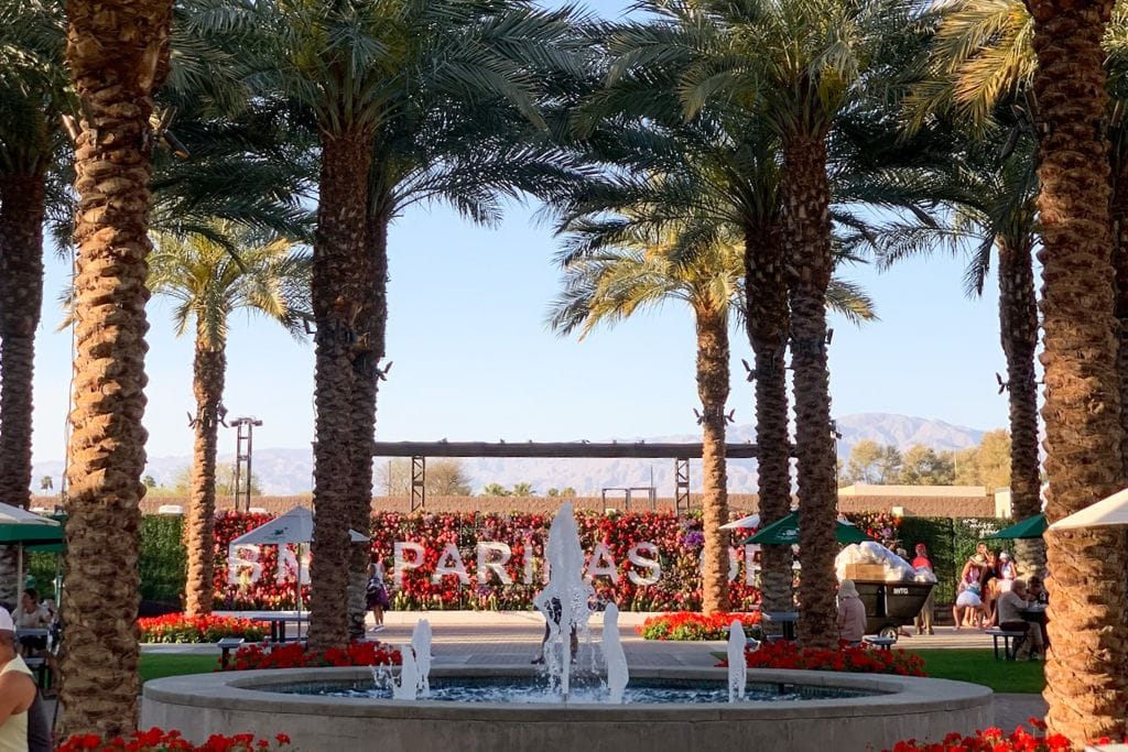 A picture of the colorful flower wall that reads "BNP Paribas Open,". There are also lots of palm trees and a fountain in the center on the Indian wells tennis tournament grounds.