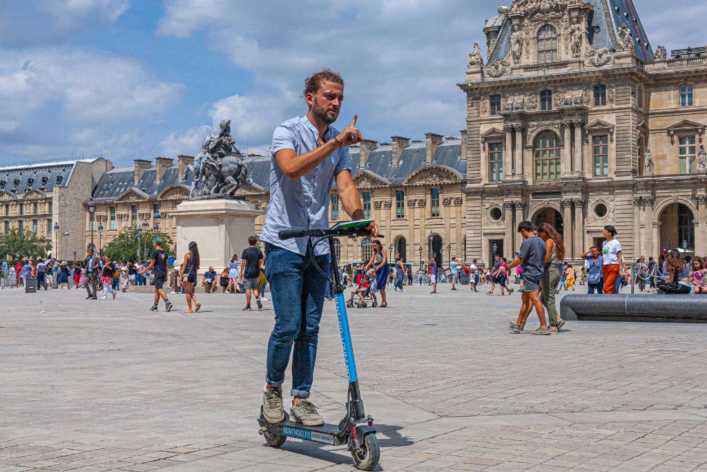 A picture of a bunch of people walking and a french man on an electric scooter. To avoid Paris Syndrome, expect lots of crowds and walking!