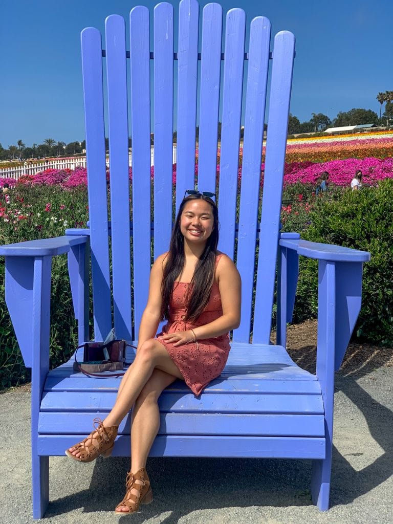 A picture of Kristin sitting on a massive blue chair in the Illusion Garden at the Carlsbad Flower Fields.