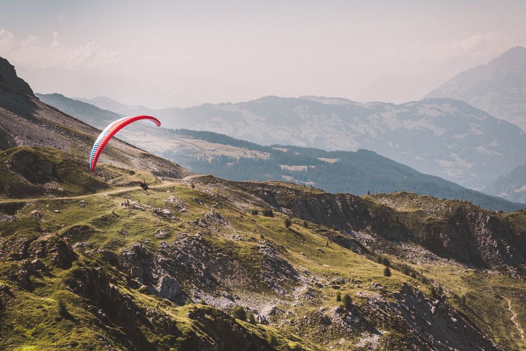 A picture of a person paragliding in Davos, Switzerland. You can see the lush mountainside as the paraglider descends into the valley.