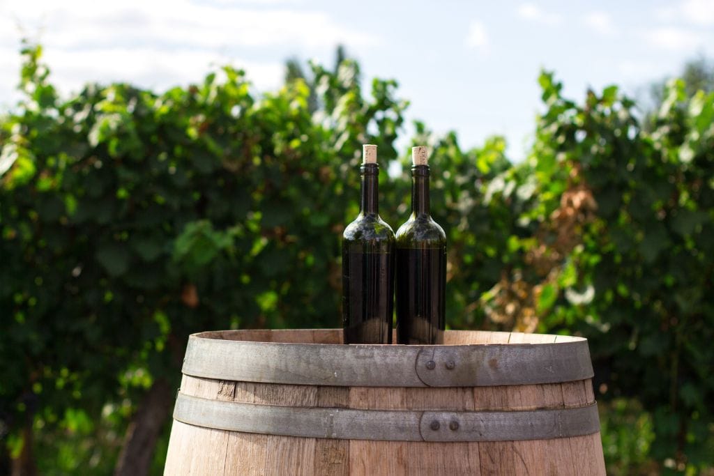 A picture of two wine bottles on top of a barrel. 