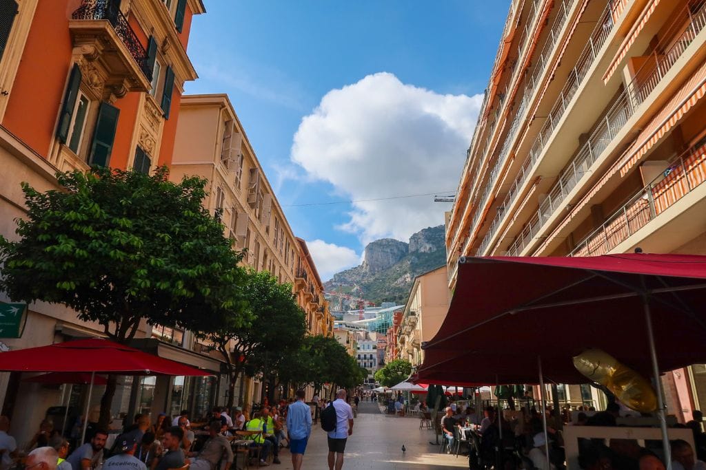 A picture of one of the narrow streets filled with restaurants and shops in Monaco. Opt to eat from a small shop instead of a fancy restaurant if you want a less expensive visit to Monaco.
