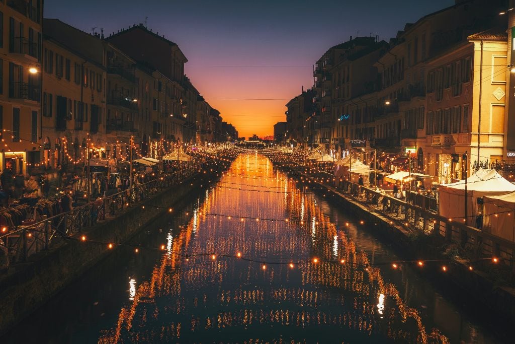 A picture of the Navigli district at night with lots of lights and a beautiful sunset.