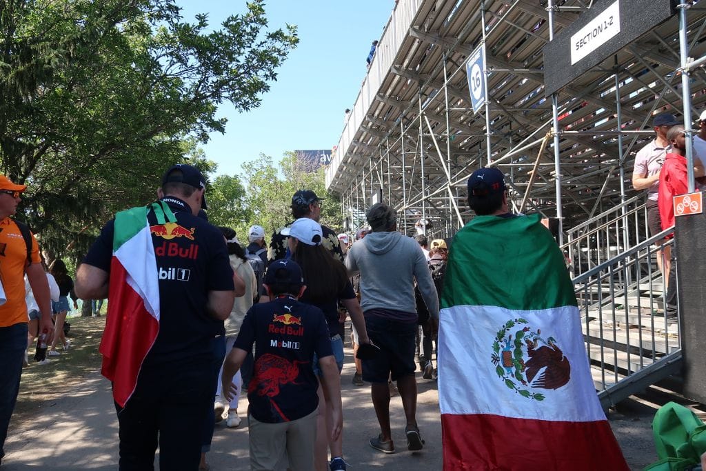 A picture of several f1 fans wearing redbull gear and holding the Mexican flag. F1 TV is worth it because you can watch the onboard of your favorite driver.