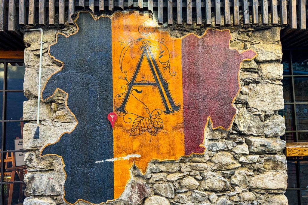 A picture of a wall mount in the shape of Andorra with the country's flag colors painted on top. Maybe people don't realize that Andorra is not expensive to visit from France or Spain.