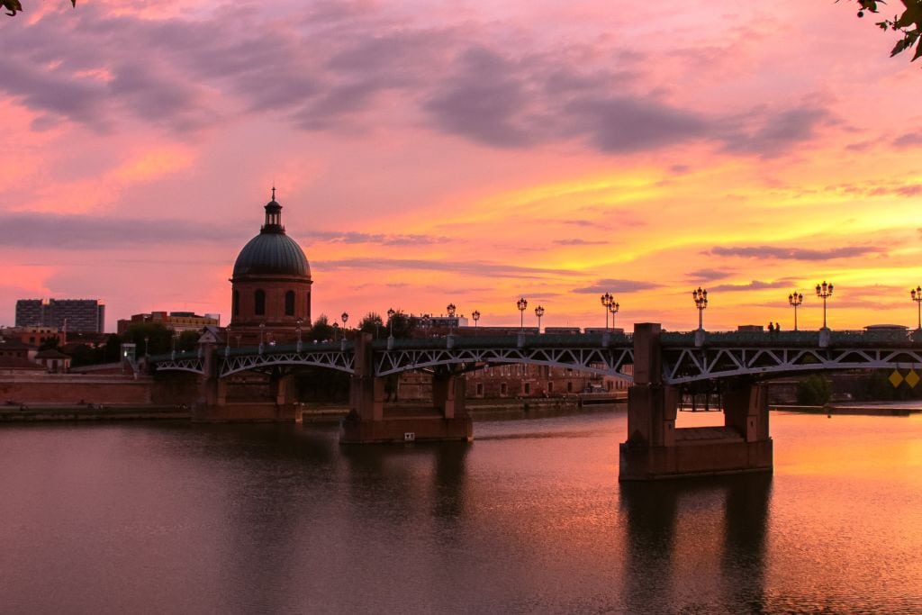 A picture of Toulouse with a beautiful pink and purple sunset in the background. Explore Toulouse's night life with a wine tour from Toulouse.