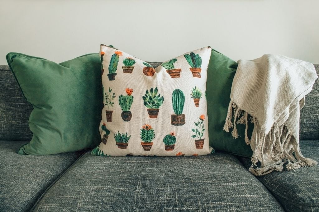 A picture of a couch with green throw pillows and a soft white blanket draped over the edge.