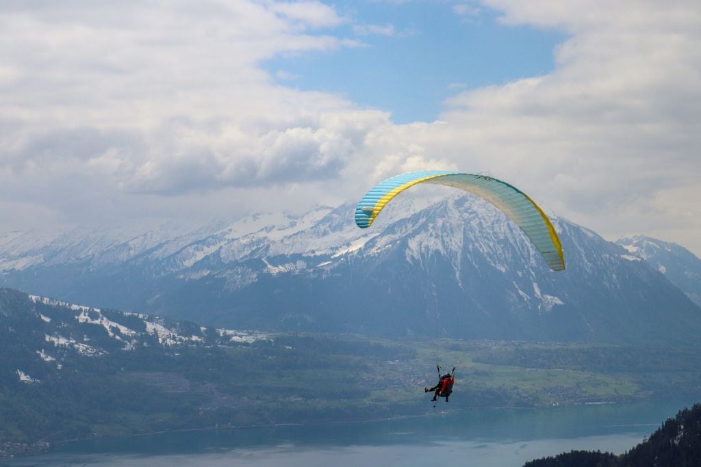 A picture of a person paragliding with snow capped mountains in the background. There are tons of captions you can do for Instagram posts about paragliding.