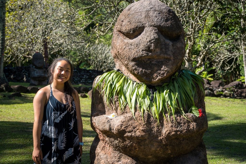 A picture of Kristin smiling next to a giant statue at Marae Arahurahu in Tahiti. There are some free excursions available around French Polynesia to keep your trip on the less expensive side!