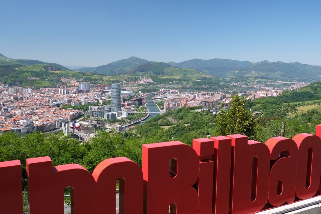 A picture of Bilbao's city scape and the surrounding verdant mountains as seen from the top of Monte Artxanda. 