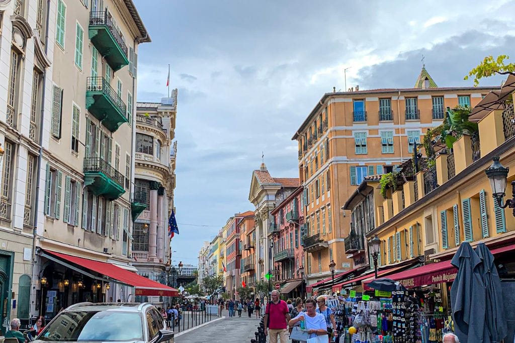 A picture of busy streets of Nice with sidewalk cafés on the right.