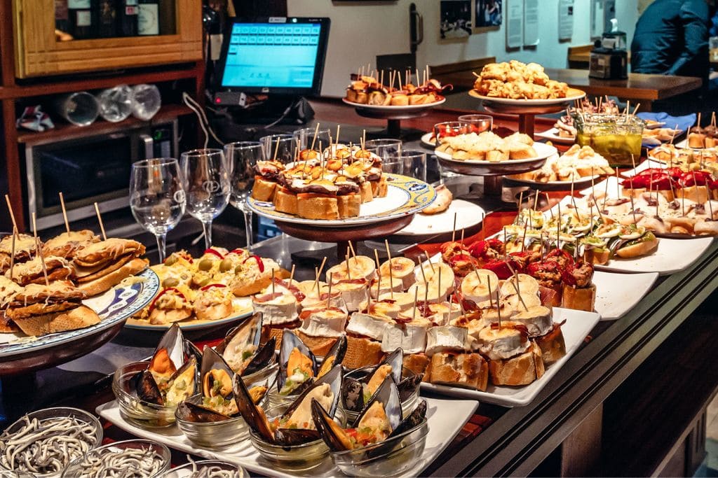 A picture of an assortment of pintxos at a bar! All of the food tours in San Sebastian including sampling lots of pintxos!