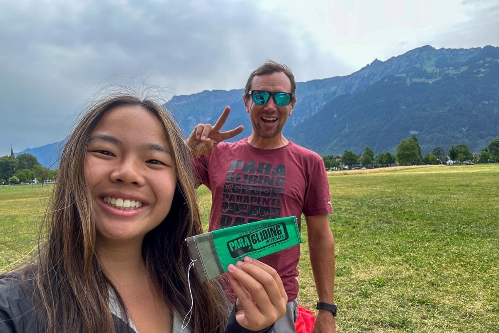 A picture of Kristin and her pilote smiling after an adrenaline-filled paragliding flight in Interlaken!