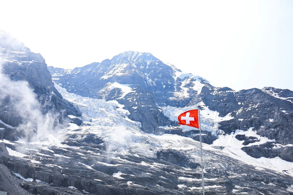 The snow capped mountains around Jungfraujoch with a bright red Swiss flag flying high. Grindelwald is worth visiting if you want to ascend to the top of Europe. 