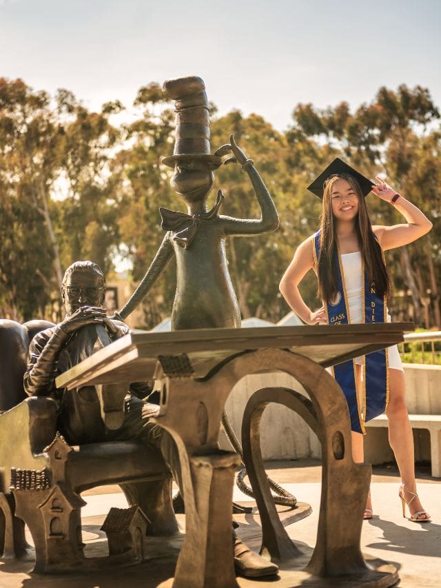 A picture of Kristin standing next to a bronze statue of Giesel and Dr. Seuss from her graduation photoshoot.