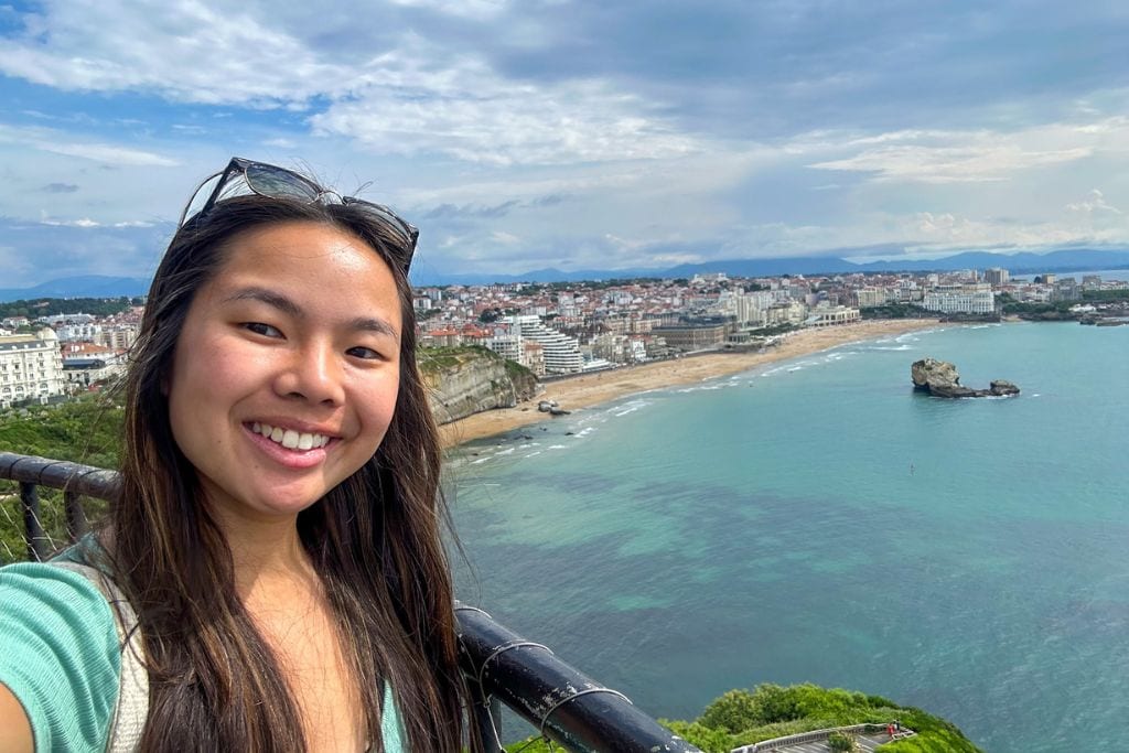 A picture of me smiling from the top of the Biarritz lighthouse and the stunning Basque coastline in the background.