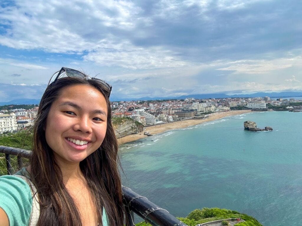 A picture of me smiling from the top of the Biarritz lighthouse and the stunning Basque coastline in the background.