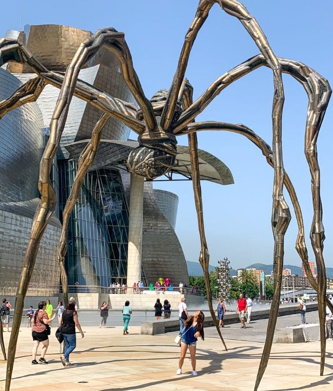 A picture of Kristin cowering underneath the giant spider art installation at the Guggenheim Museum.