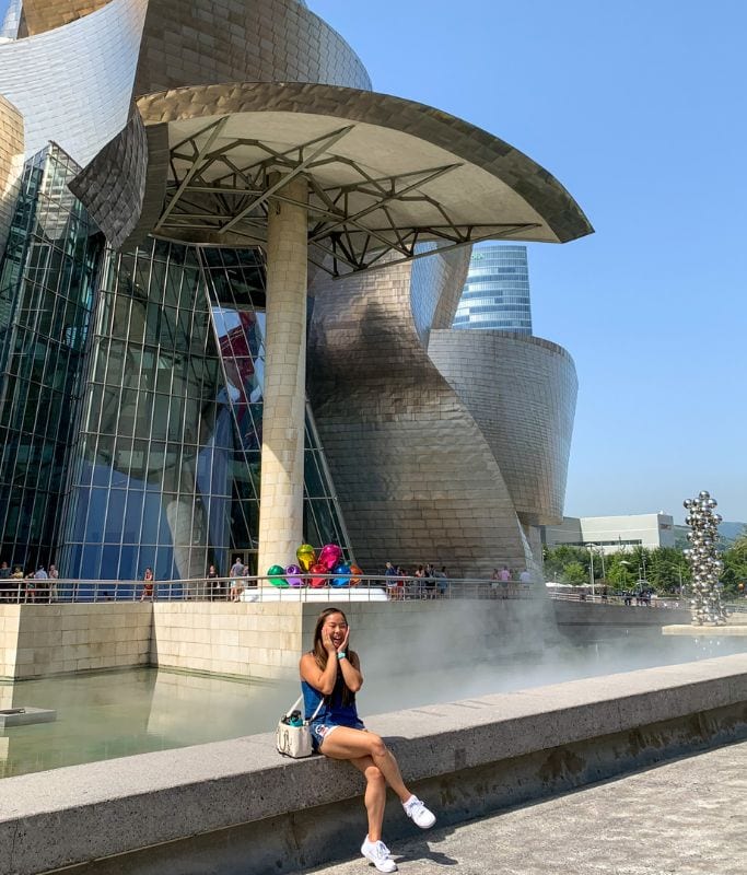 A picture of Kristin sitting in front of the Guggenheim Museum in Bilbao