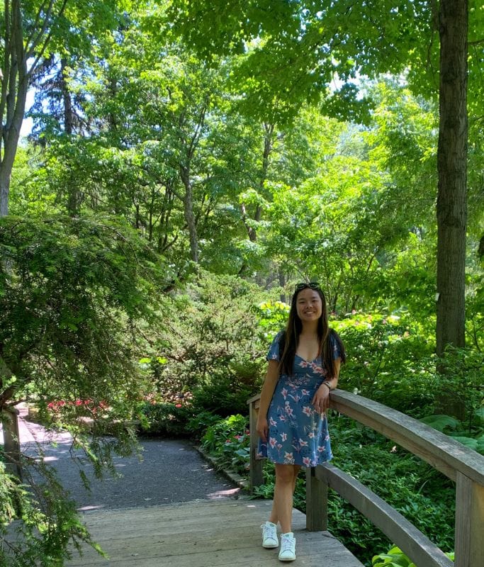 A picture of Kristin leaning against a wooden rail in the Kristin at the Montreal Botanical Gardens.