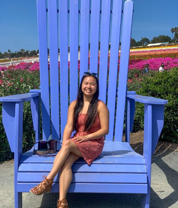 A picture of Kristin sitting on a massive blue chair in the Illusion Garden at the Carlsbad Flower Fields.