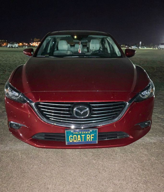 A picture of a red car with a cool license plate that reads, "GOAT RF" at the Indian wells tennis tournament parking lot.