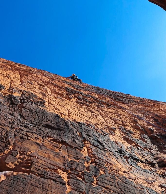 A picture of Kristin sport climbing. In the picture, she has reached the top of her route. 