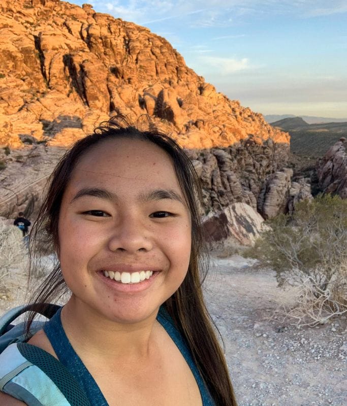 A picture of Kristin smiling with her backpack and the beautiful red rocks in the background. Doing a bike tour through Red Rock Canyon is one of the best ways to intimately see the views!