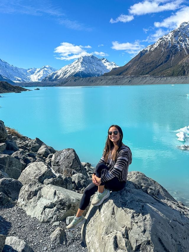 A picture of Kristin sitting on a rock next to a glacier lake in Mt Cook National Park in New Zealand